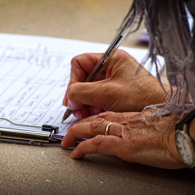 An older person signs a paper petition on a clipboard.